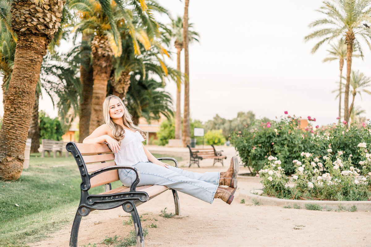 Senior Girl smiles and sits on bench at Sahuaro Ranch Park in Glendale, Arizona for senior photography session.