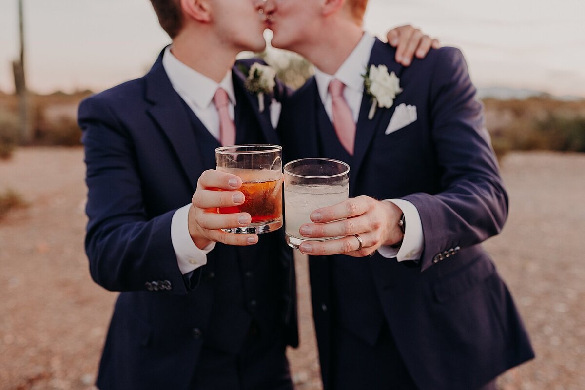 Two grooms clink glasses and share a cocktail