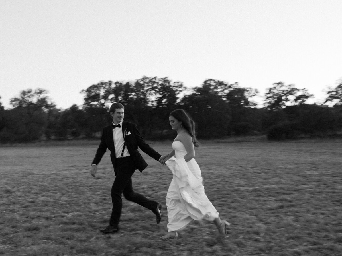 Black and white blurry image of bride and groom running through the grass