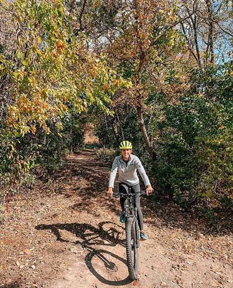 A woman biking on a wooded trail in Ohio State Parks, surrounded by lush greenery and tall trees.