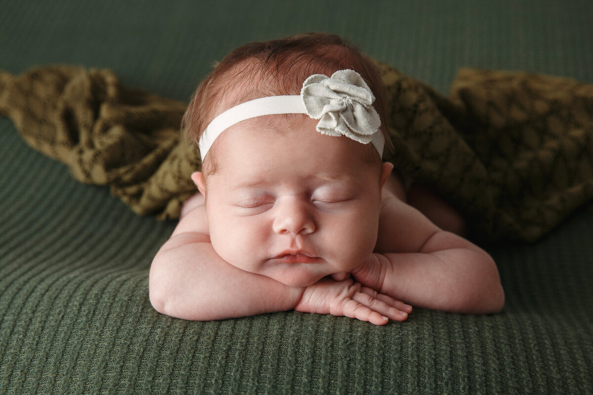 Newborn baby laying on Tummy and faceing the camera wearing a white headband