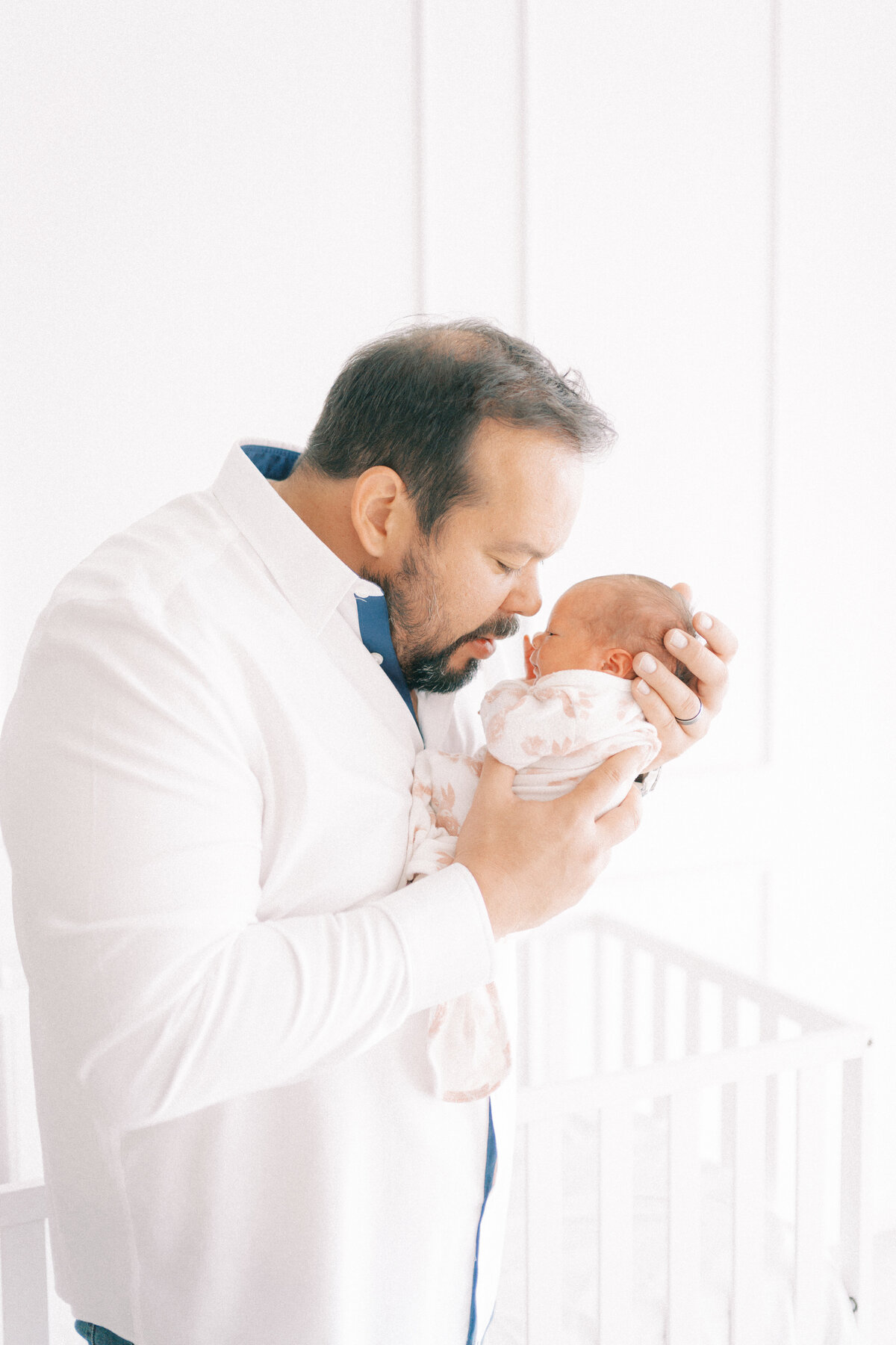 dad in white shirt holding newborn baby gently pressing his nose to her nose