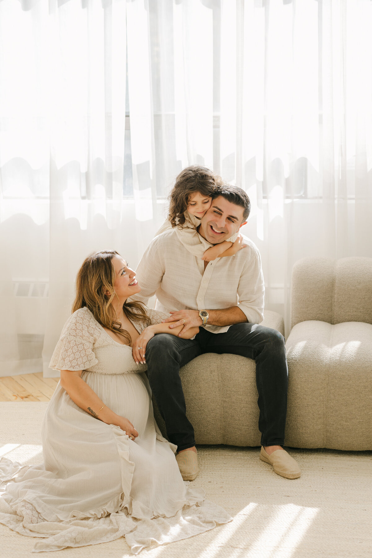 Little girl hugging her dad while her pregnant mother is smiling at them in a Toronto studio