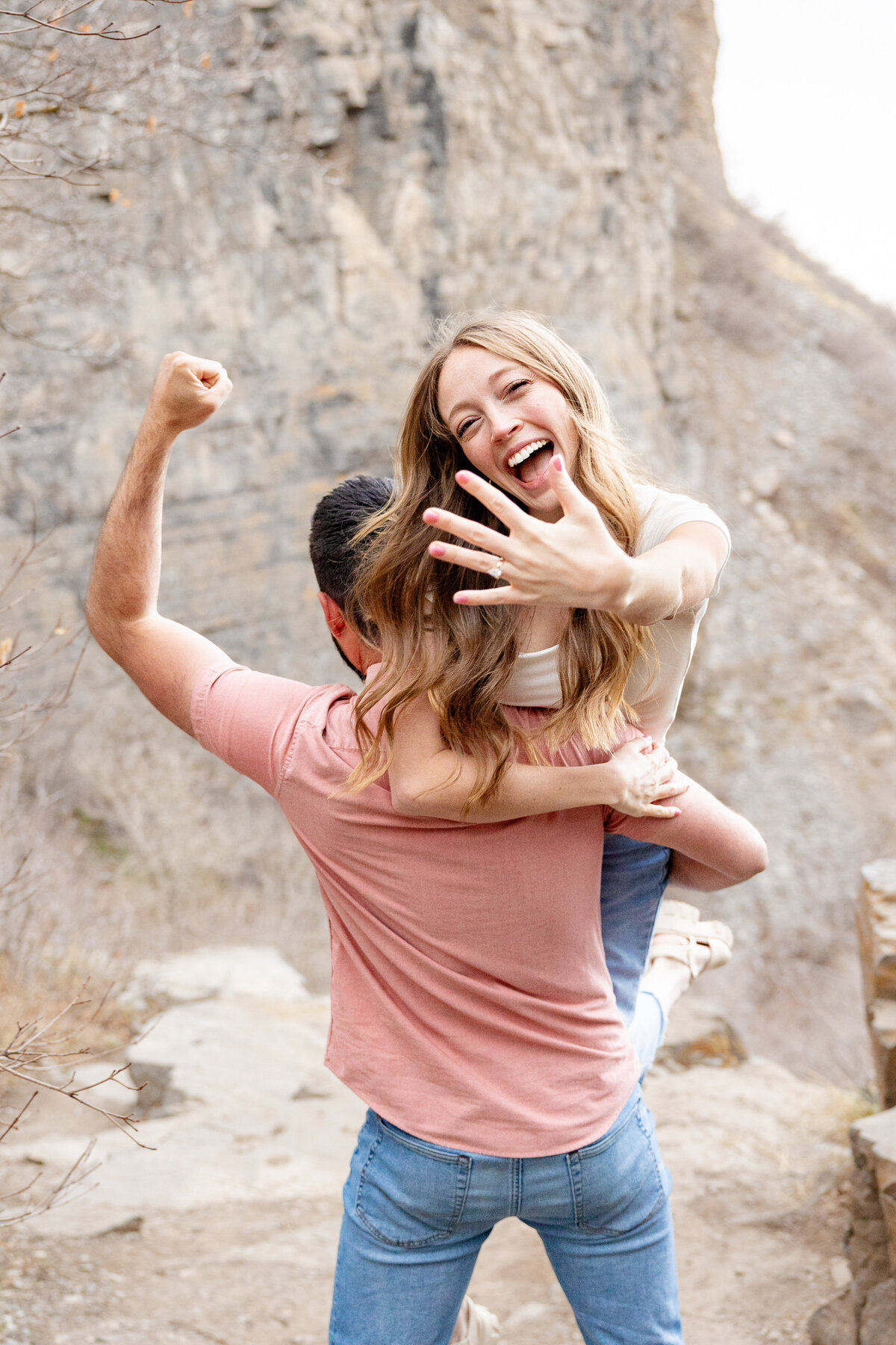 Bride-to-be being lifted by her fiancé, joyfully showing her engagement ring to the camera with a big smile on her face in Orem, Utah.