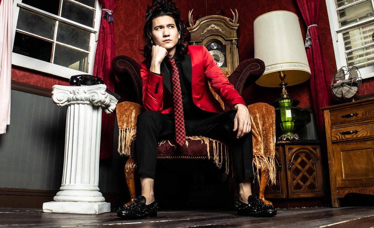 Male musician portrait Sean Harper wearing red suit jacket sitting with hand on chin looking left