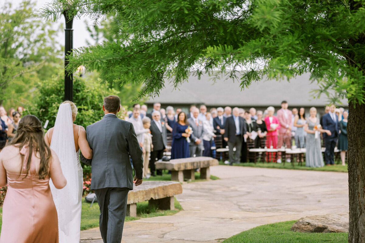 bride-and-dad-approaching-ceremony-with-guests-in-background