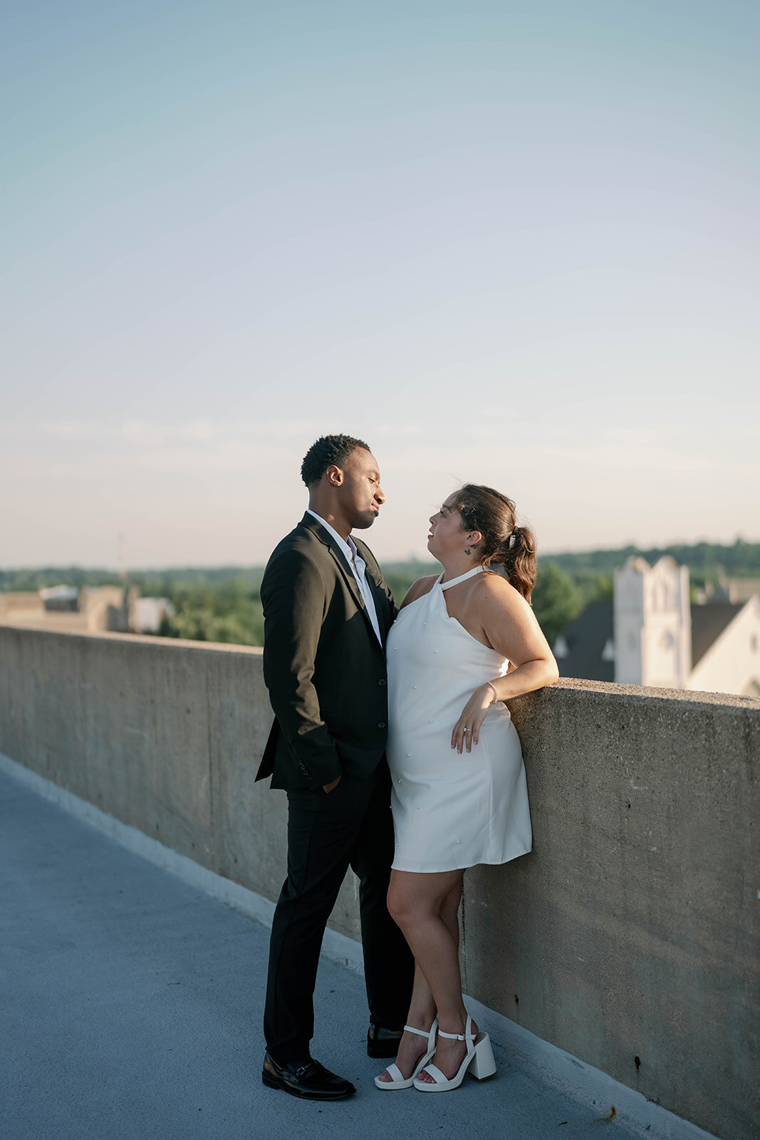 Dramatic rooftop engagement portrait overlooking downtown Kalamazoo skyline.