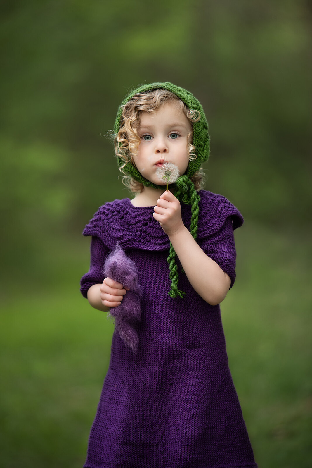 girl blowing a dandelion in purple and green outfit
