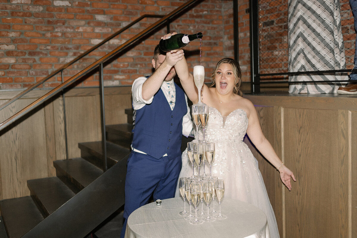 Bride and groom poor champagne on the top of their champagne tower at their wedding reception.