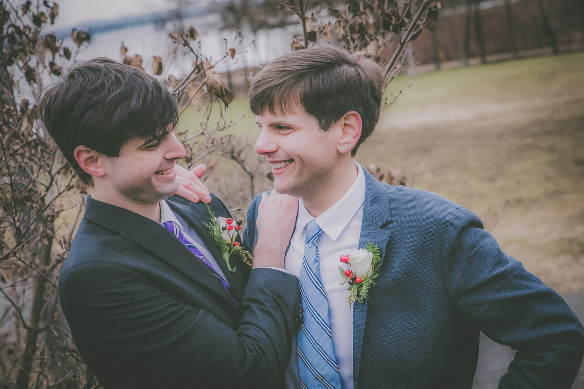 Grooms look at each other and smile in park.
