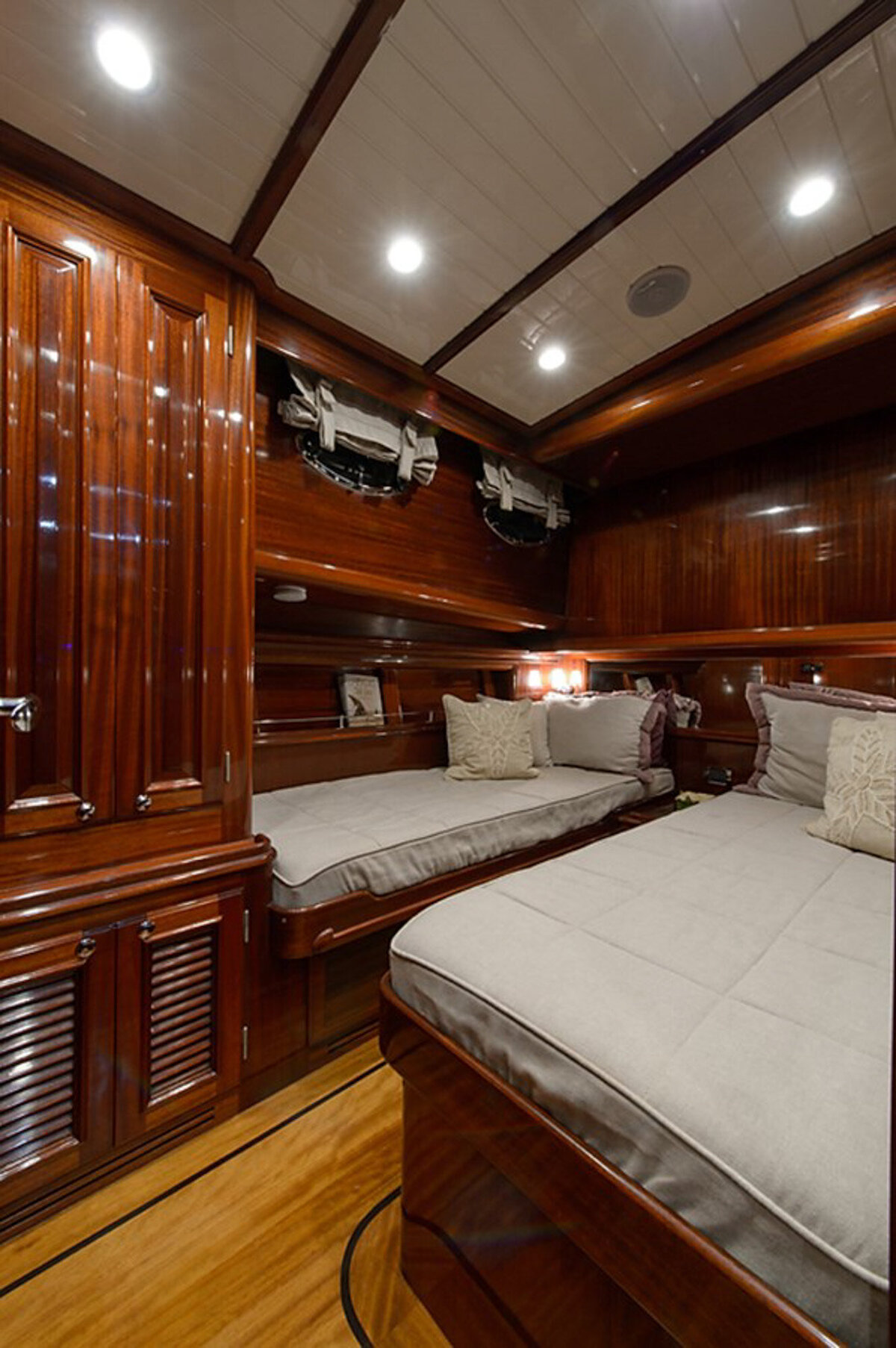 cozy, luxurious cabin room on a yacht features rich wood paneling, two single beds with beige cushions and pillows, and soft ambient lighting