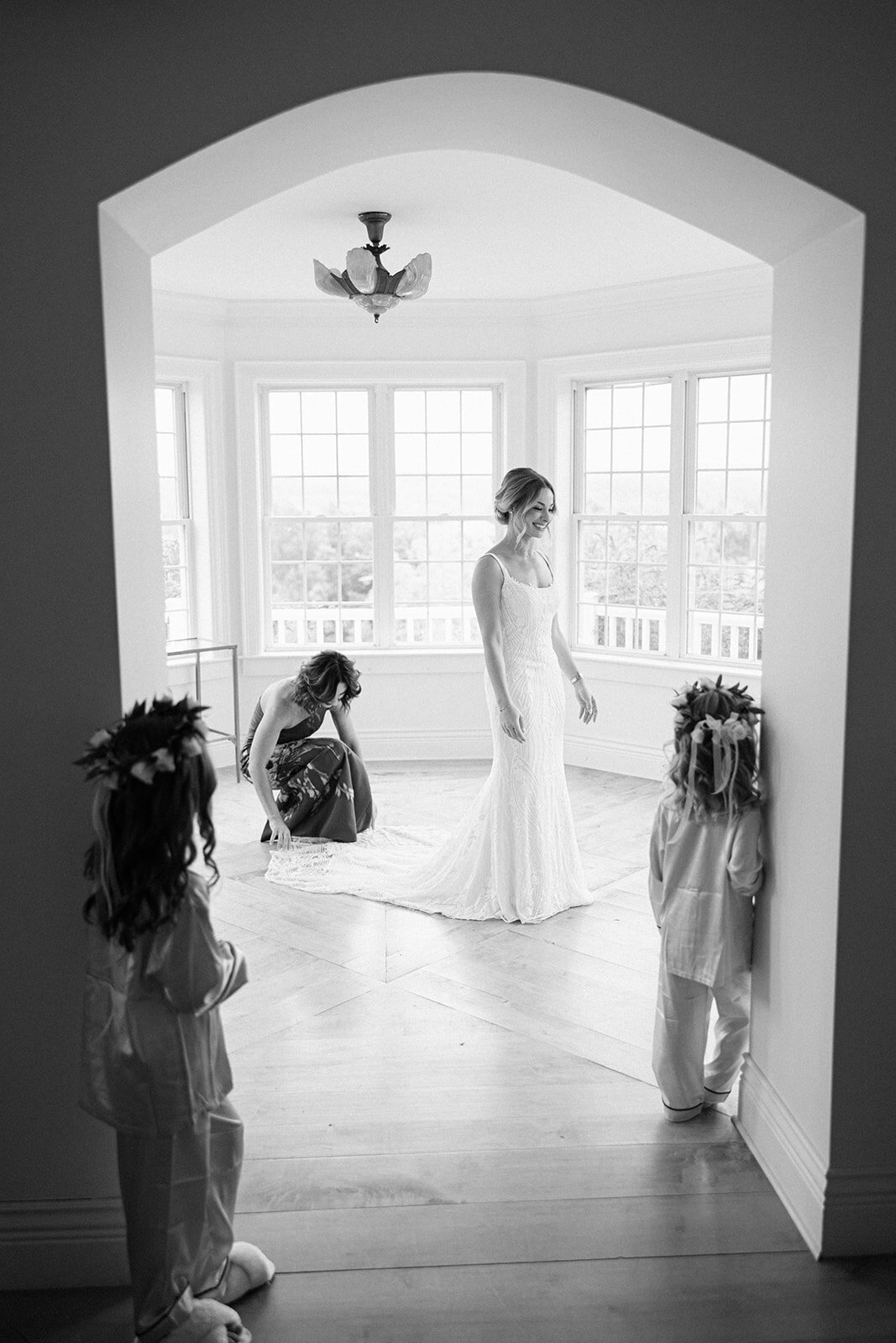 Bride standing in room with girl fixing veil and little girls looking at her at Crispin Hill on Keuka Lake Fingerlakes, NY