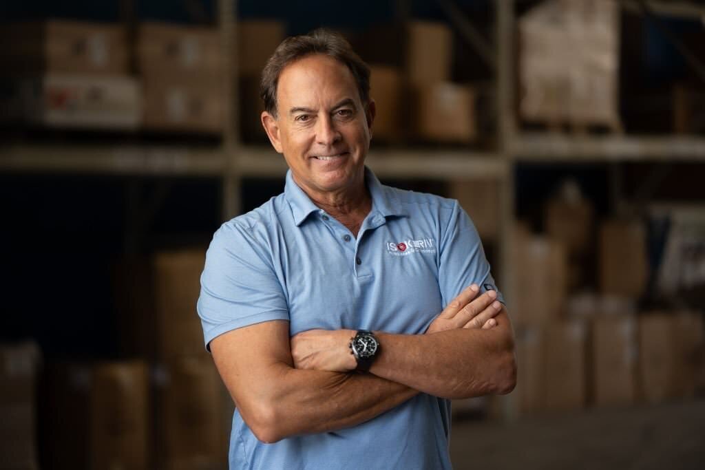 A-confident-man-in-a-blue-polo-shirt-stands-with-arms-crossed-in-a-warehouse-full-of-boxes