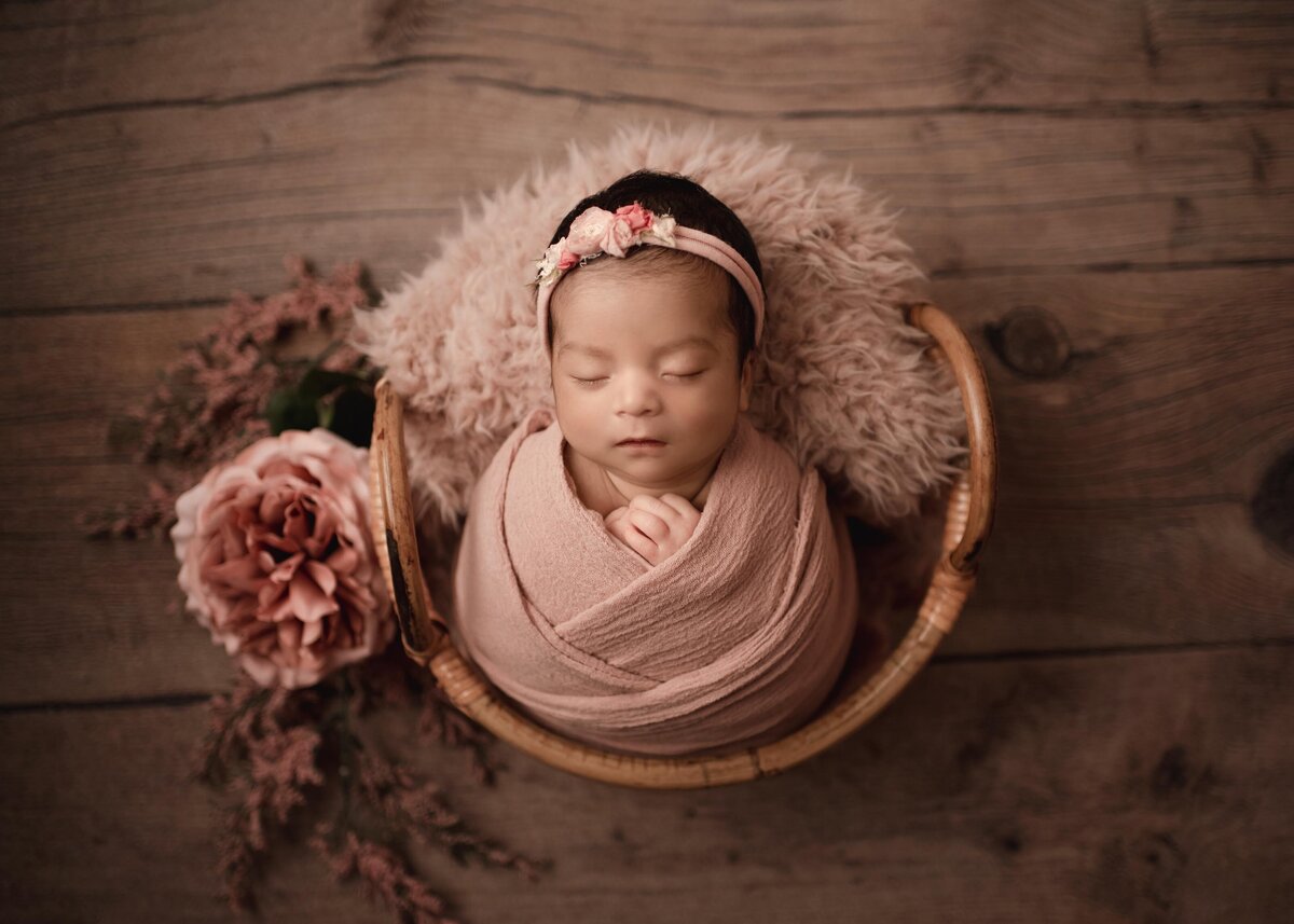Newborn baby girl peacefully sleeping wrapped in dusty rose wearing floral headband