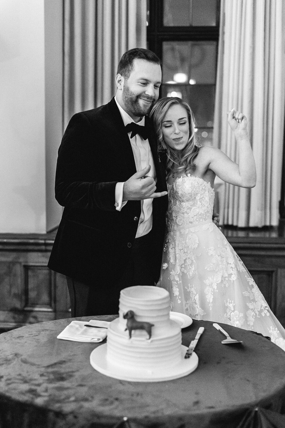 Black and white photo of bride and groom standing happily in front of their  wedding cake