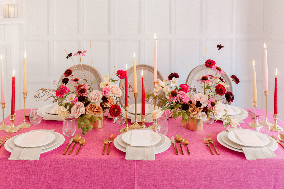 Centrepieces of bold pink and red flowers on a bright tablecloth at a Livart wedding.