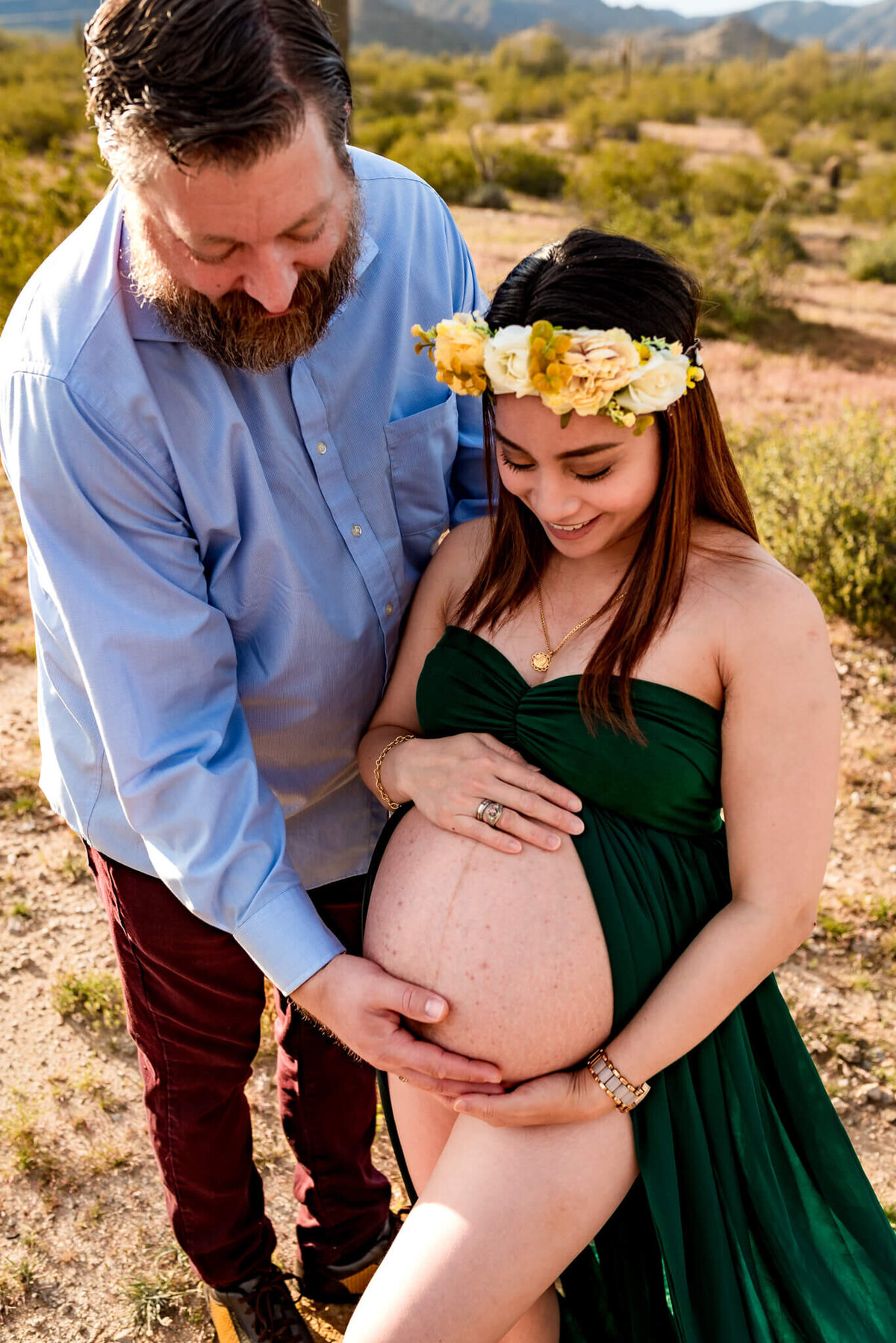 Maternity portrait of parents holding baby bump with split dress exposing stomach.