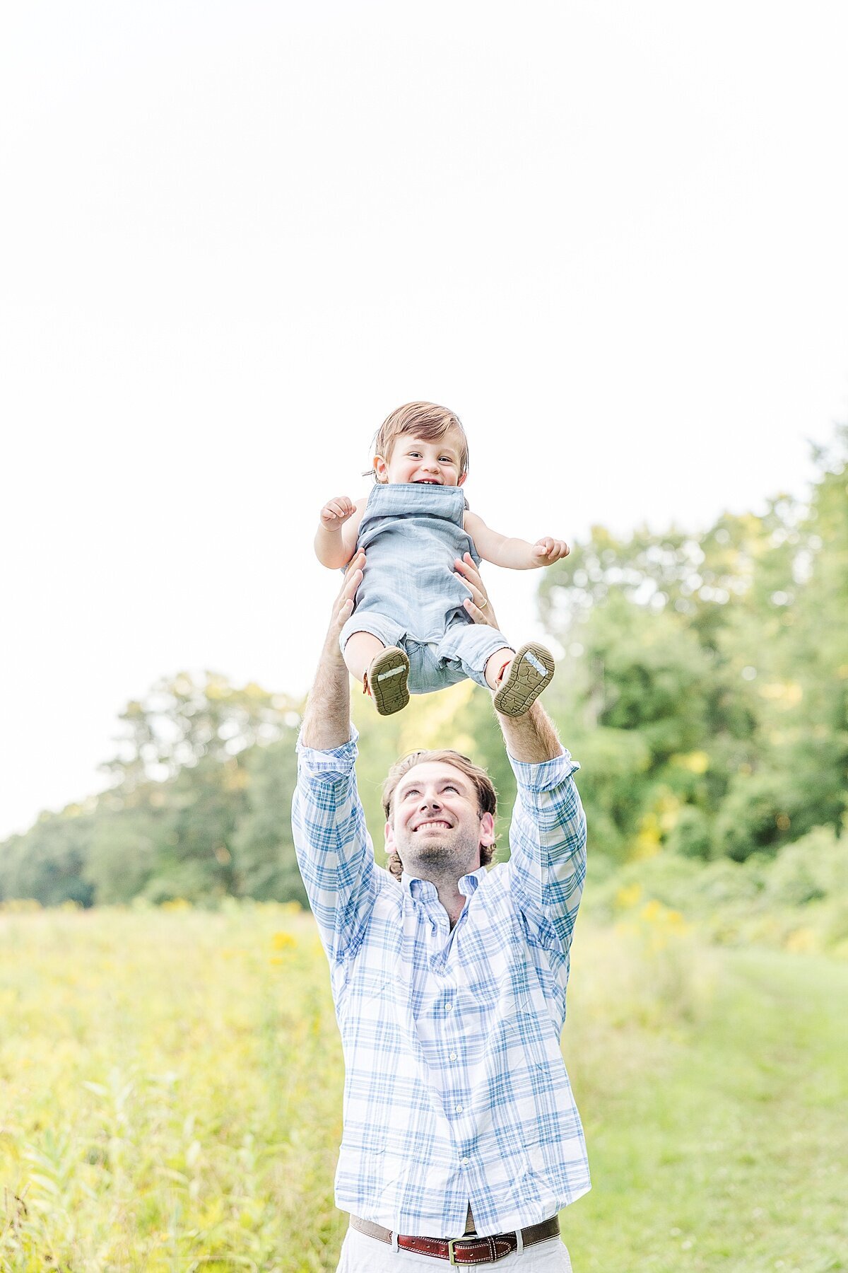 father holds son above his head during Family photo session with Sara Sniderman Photography at Heard Farm in Wayland Massachusetts