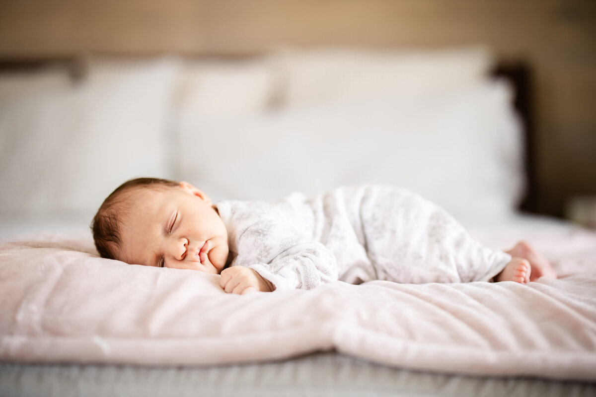 Baby girl sleeping on pink blanket on parent's bed