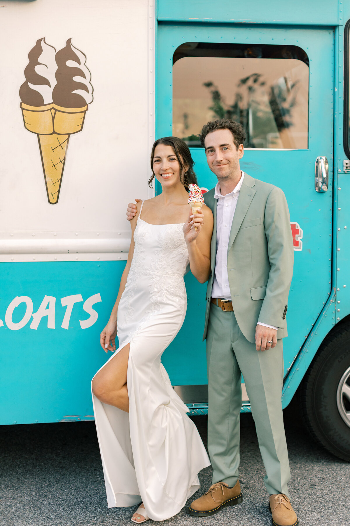 Bride in Bridal Chateau gown and groom in Indochino suit posing beside teal ice cream truck outside Fetewell wedding venue.