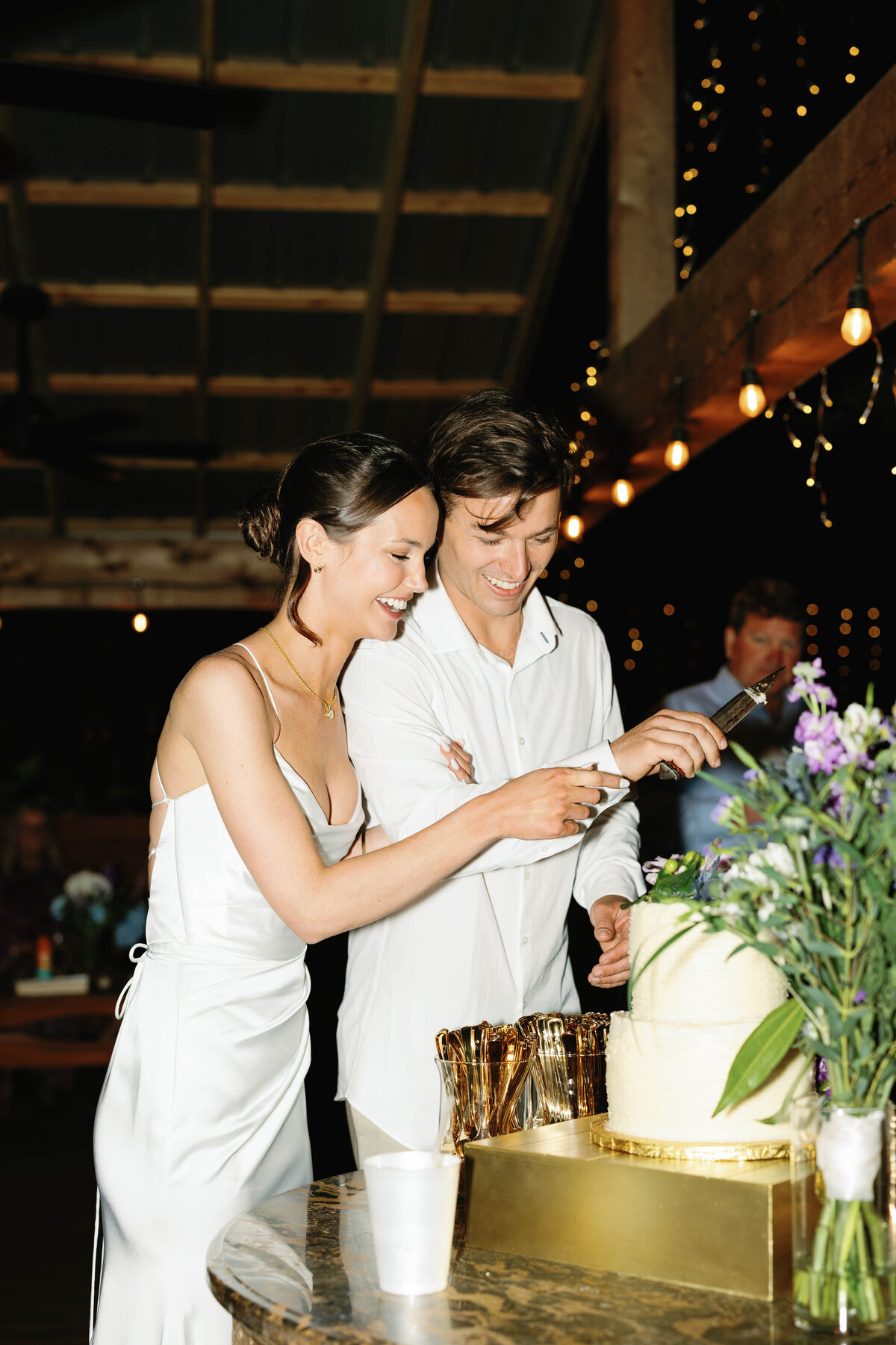 Bride and groom cut the wedding cake at their reception with smiling faces