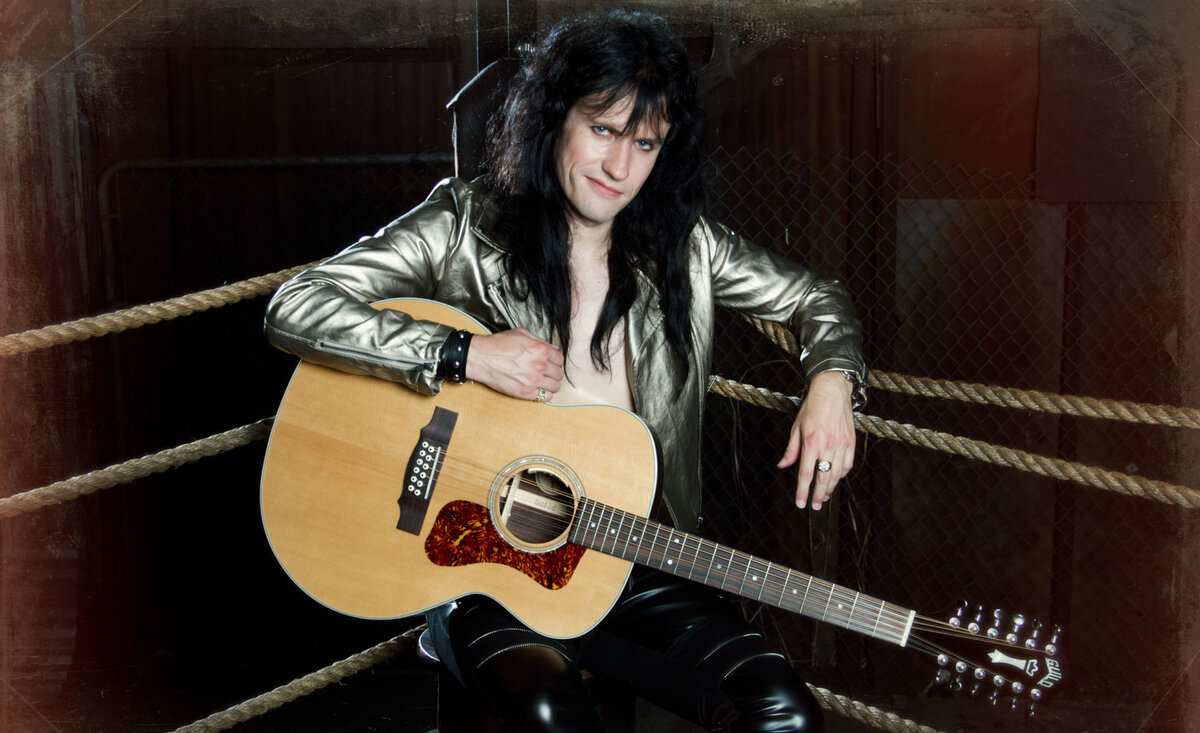 Male musician photo Rocky Kramer wearing gold jacket sitting with guitar inside boxing ring