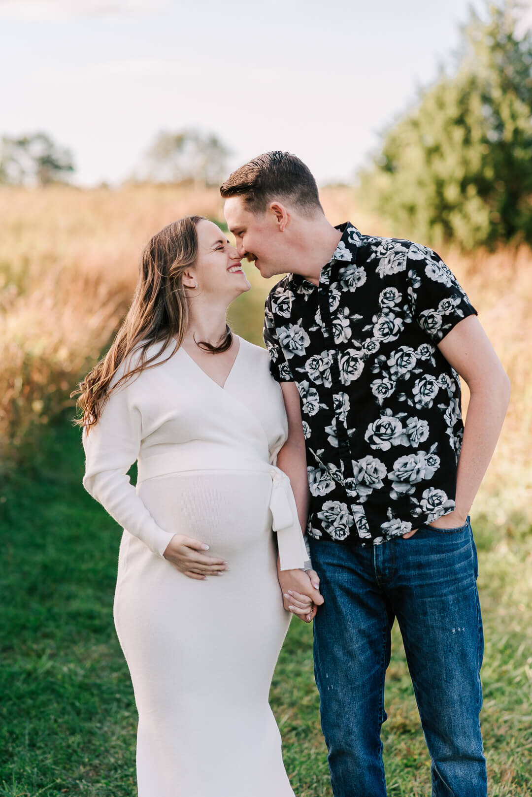 A woman in white holding her bump, grinning at her husband while standing in 48 Fields in Loudoun County