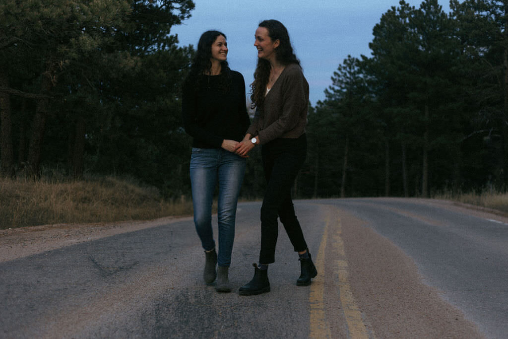 A couple holding hands and walking along an empty road.