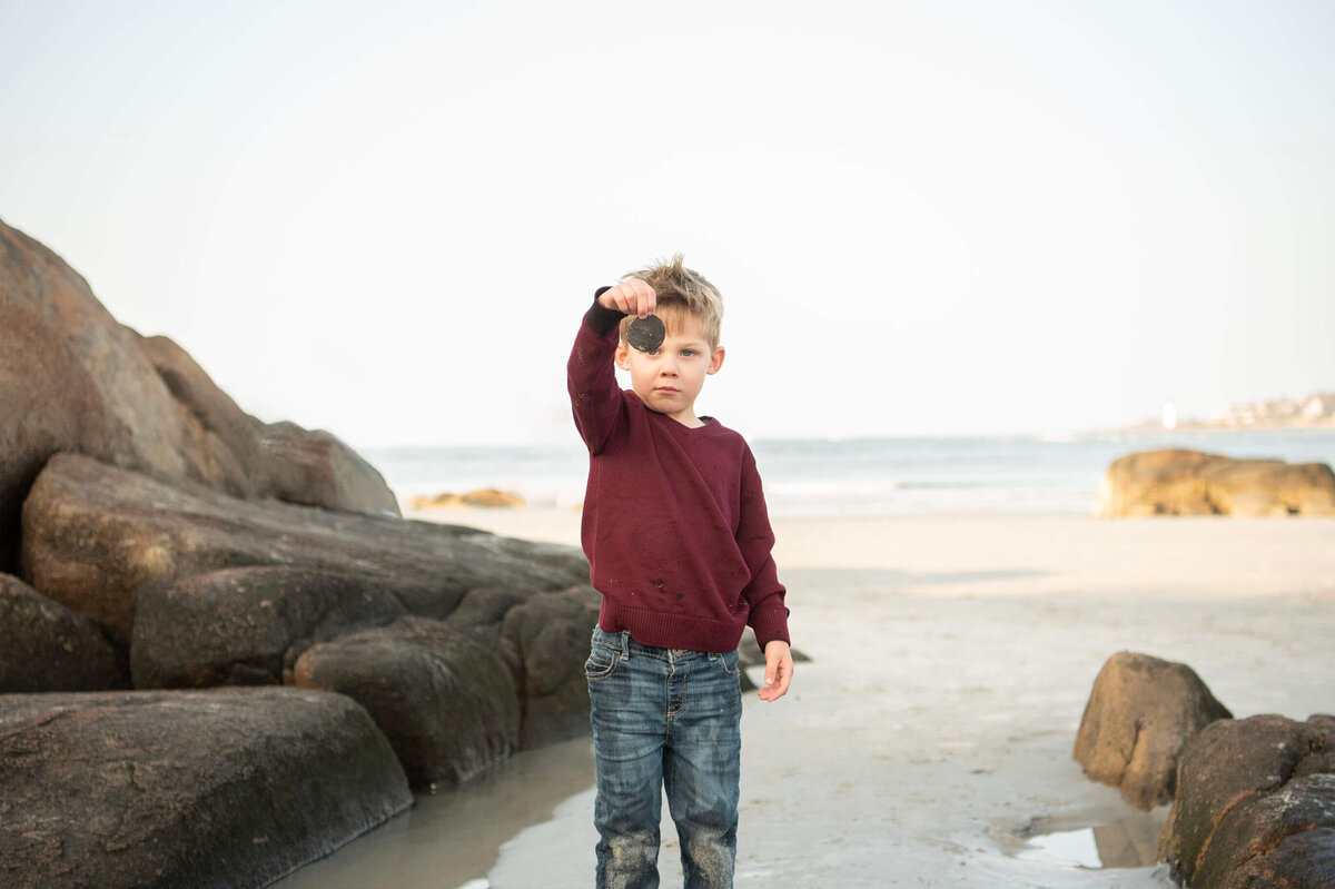 A little boy holds up a sand dollar he found during a photo session at Wingaersheek Beach.