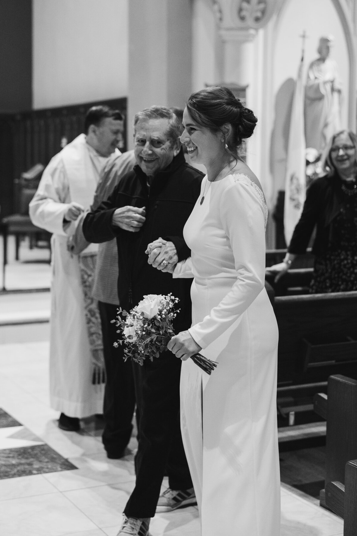 Bride smiling while walking down the aisle holding hands with her grandfather during a church ceremony at Saint Lawrence O'Toole in Brewster, NY.