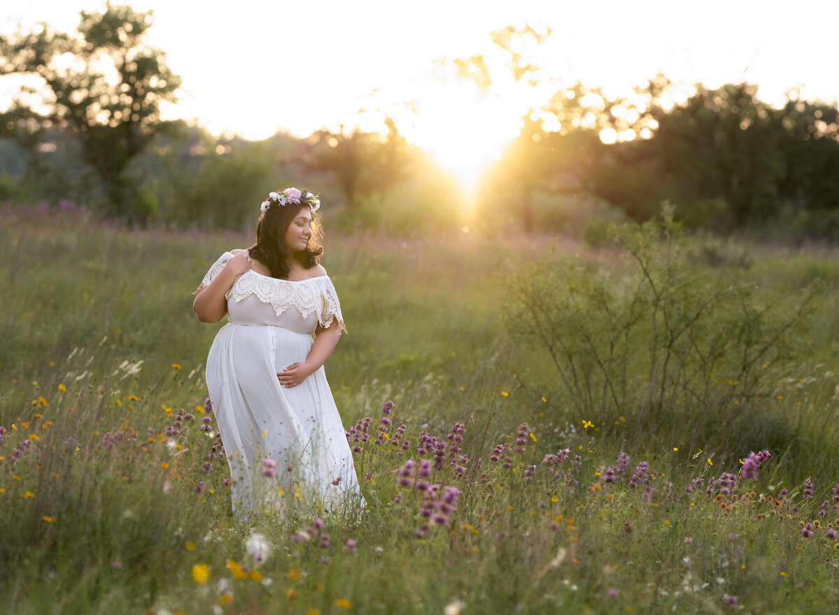 Sunset maternity photo of woman in a white dress and flower crown surrounded by wildflowers in Kyle, TX