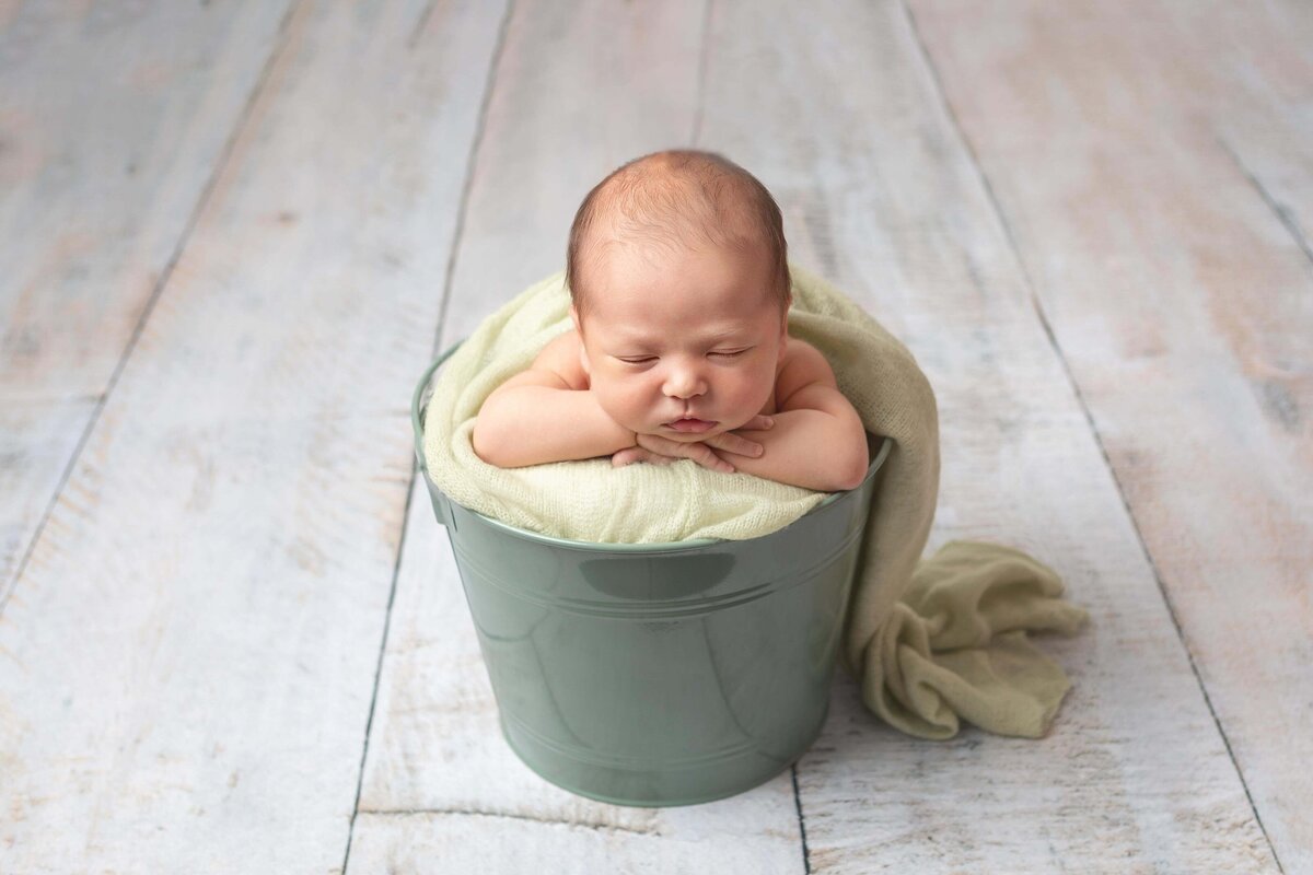 newborn baby boy in a bucket leaning on hands