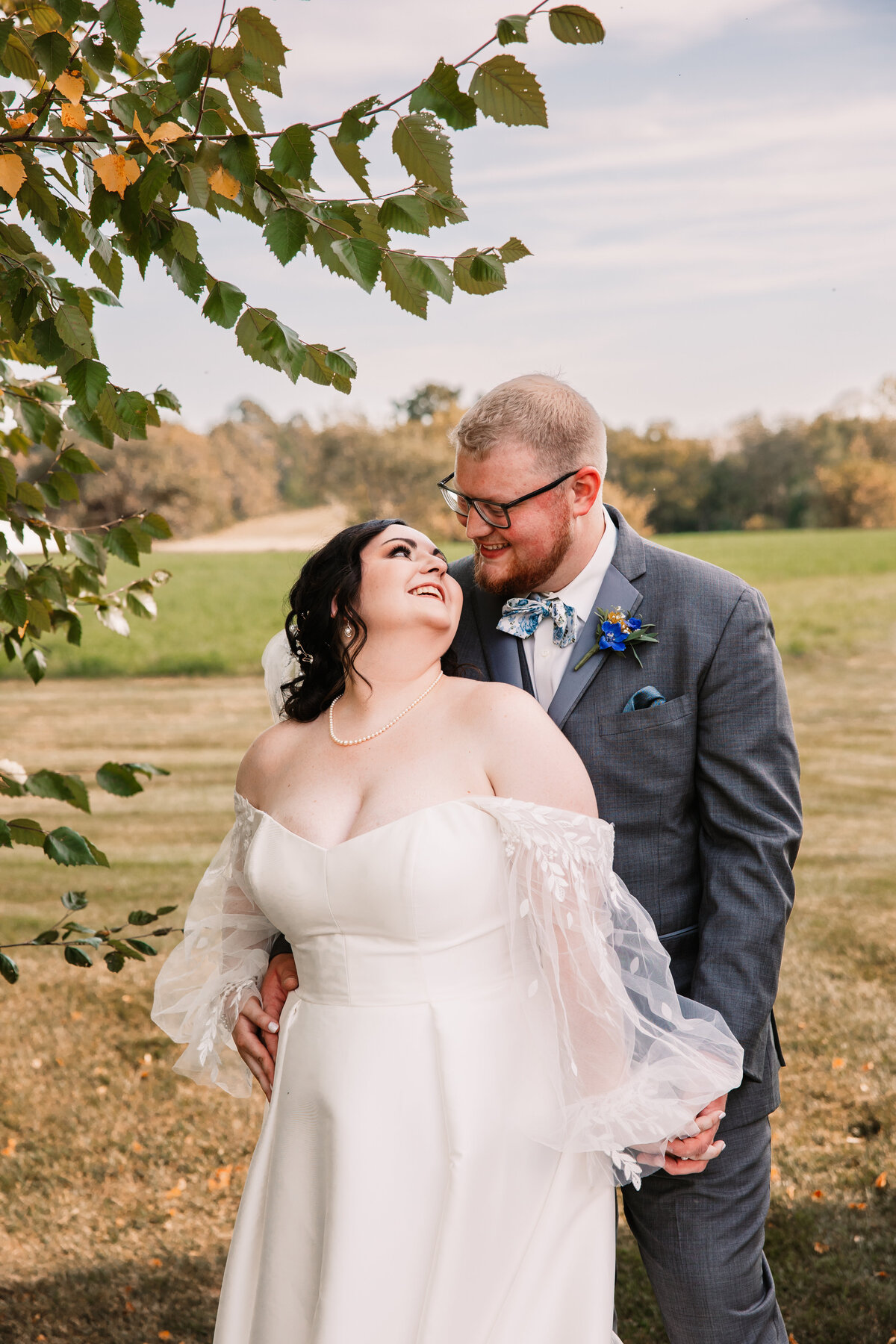 A bride snuggle her groom under a tree while looking back up at him