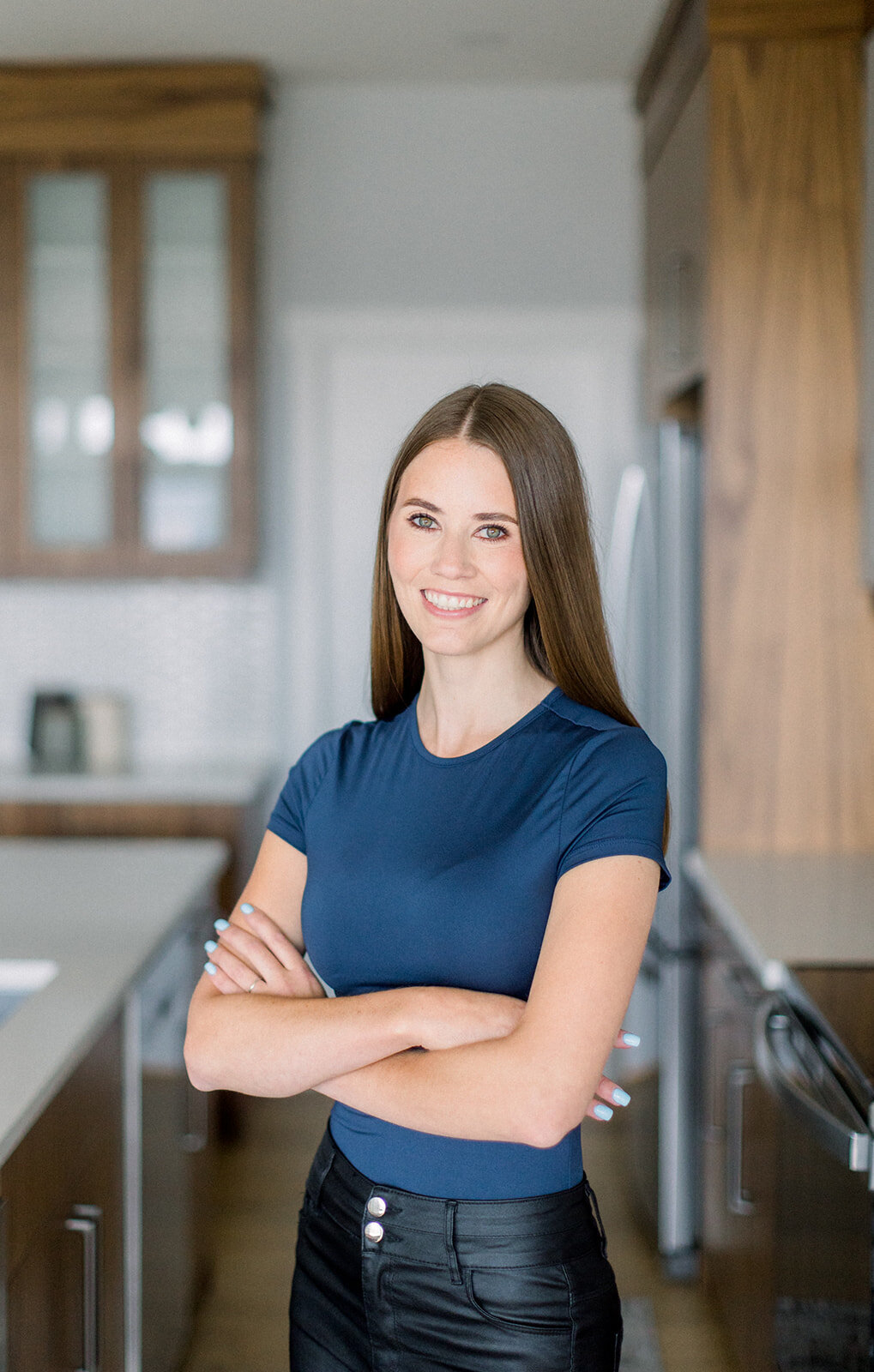 Branding headshot of a brunette woman with her arms crossed and a big smile standing in a kitchen.