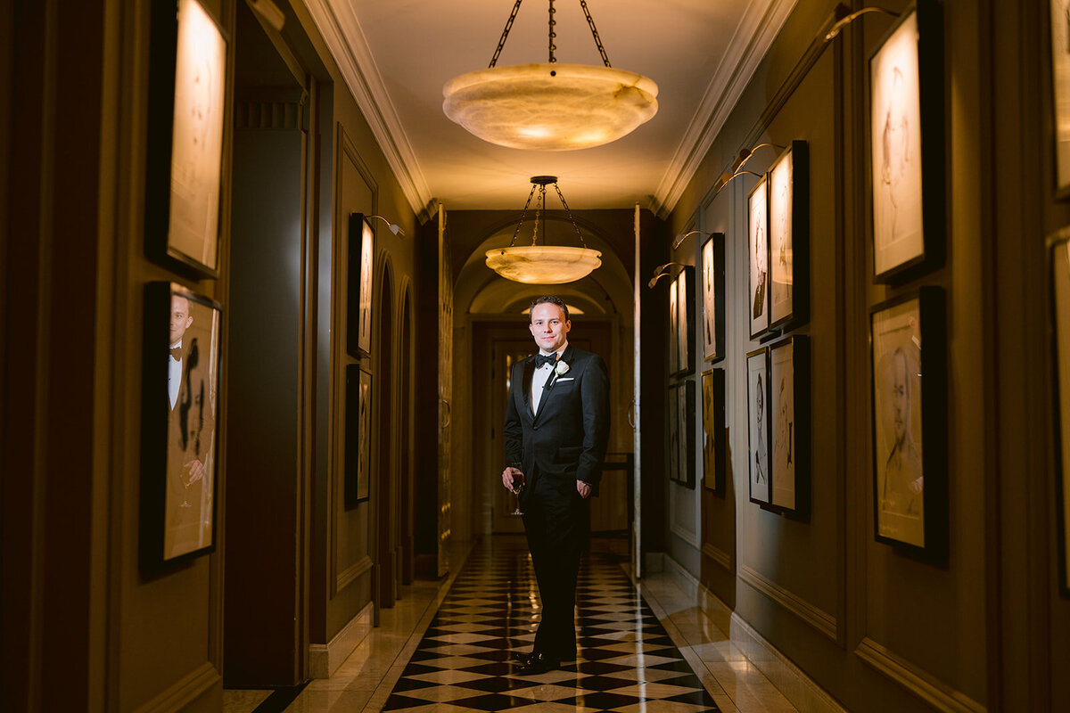 A portrait photograph of the groom in a hallway at Claridges. A dramatic lit photo