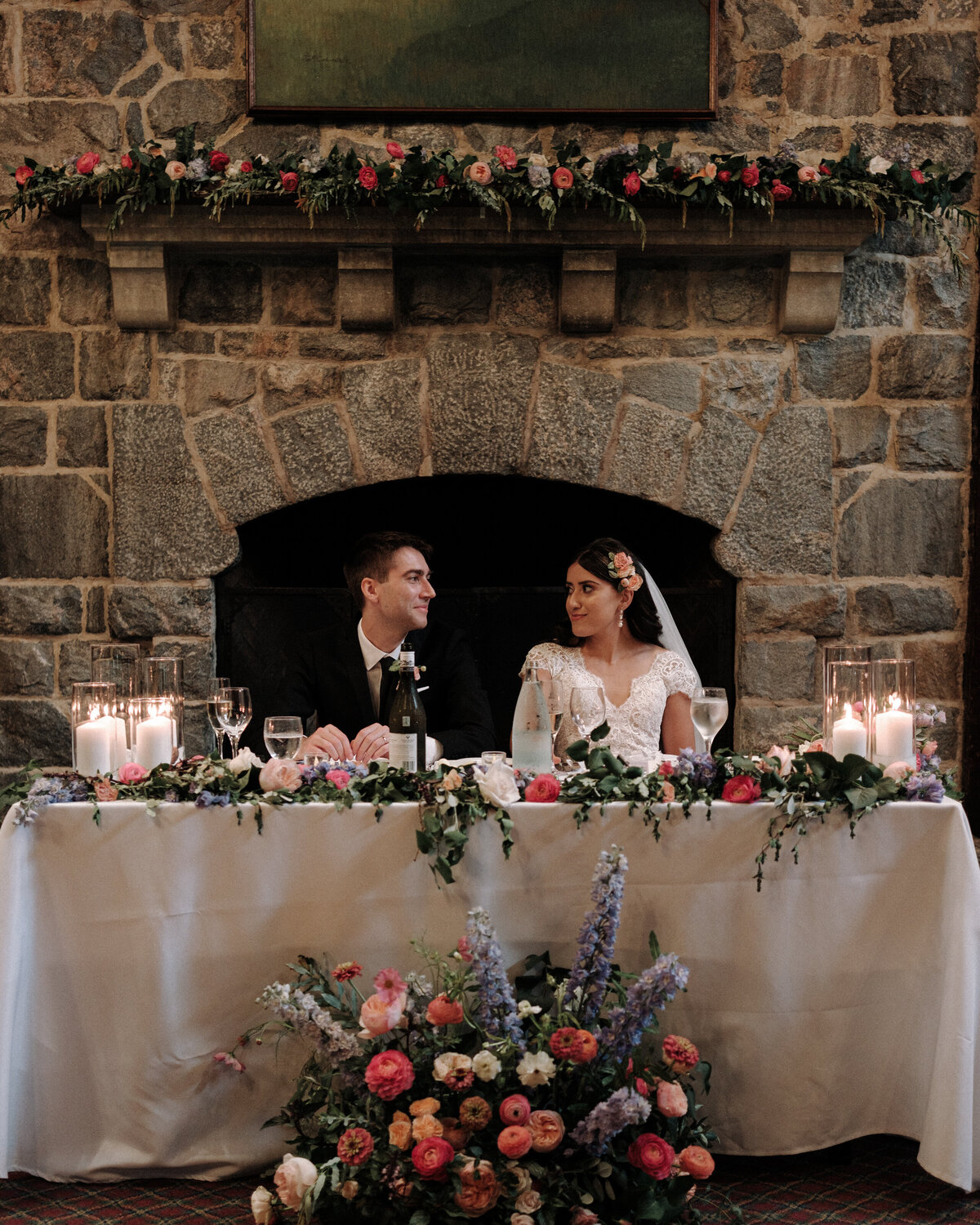 lovebirds looking at each other and their reception table in front of the fireplace