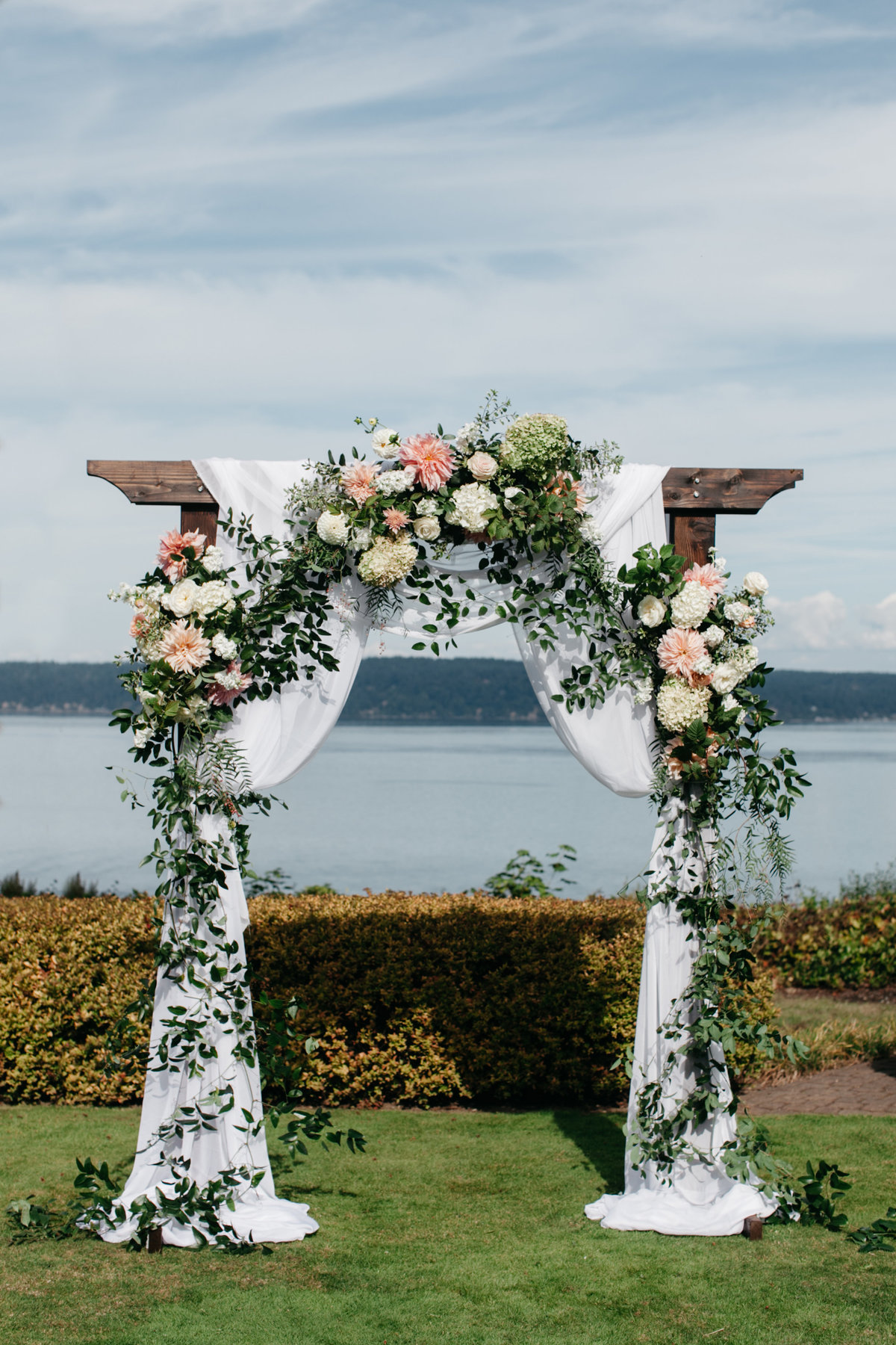 Romantic outdoor wedding ceremony arch on the water with lush summer floral.