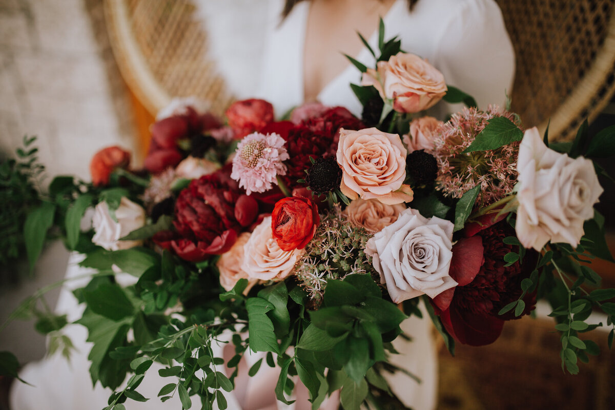 Bold Fall inspired bridal bouquet of reds, burgundy, pink, and taupe florals by The Romantiks, romantic wedding florals based in Calgary, AB & Cranbrook, BC. Featured on the Brontë Bride Vendor Guide.