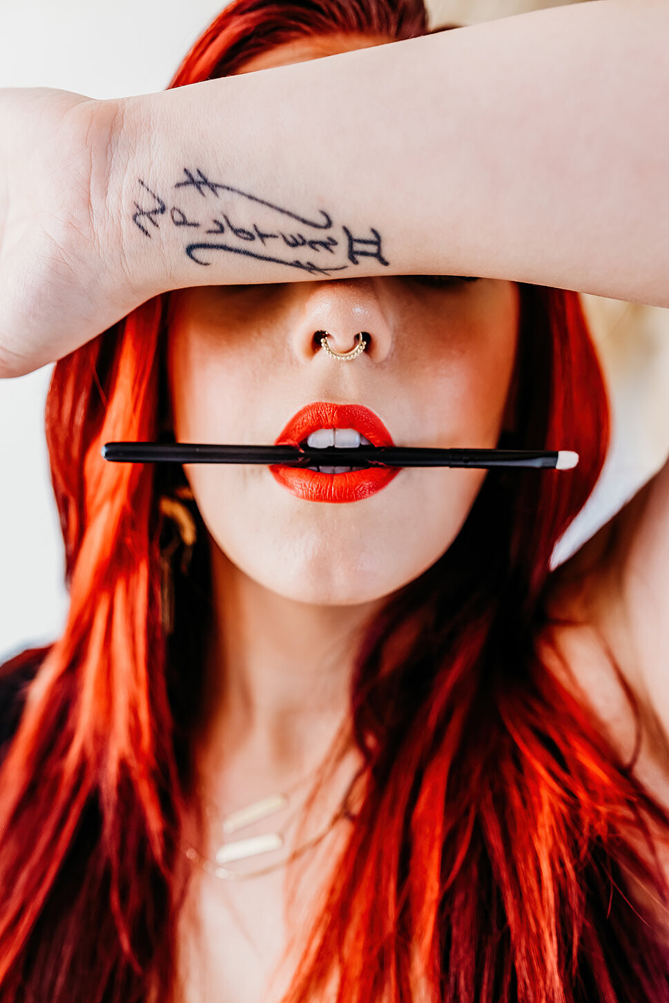 a close up of a hair and make up  artist holding a eyeshadow brush in her teeth