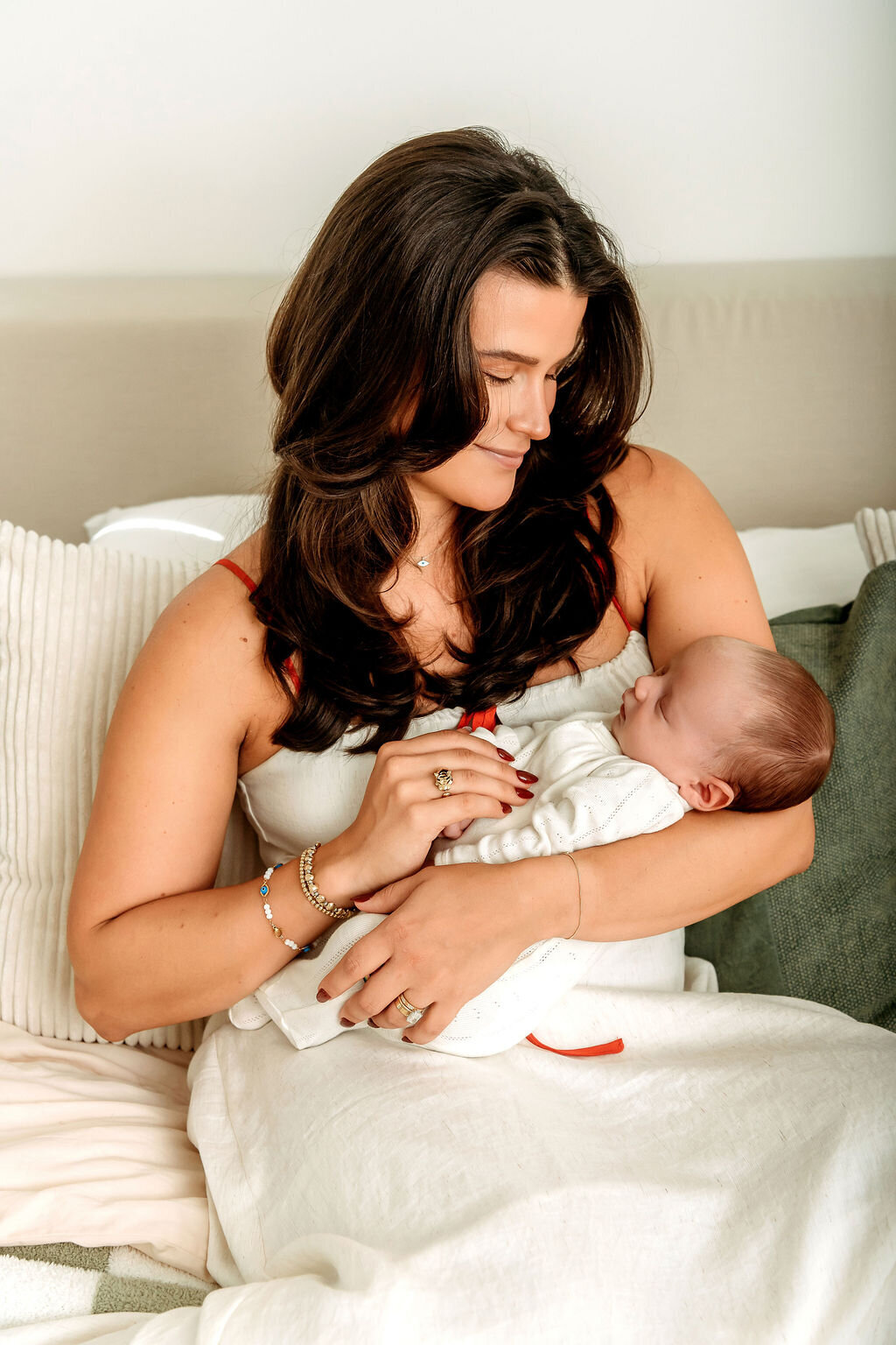 Connecticut newborn photographer specializing in lifestyle sessions captures mother lovingly gazing at sleeping baby in white outfit on bed