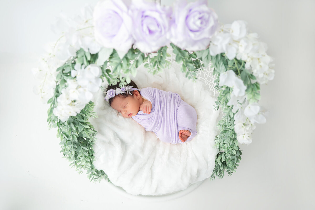 Newborn baby girl swaddled in a lilac wrap and matching colored headband. 