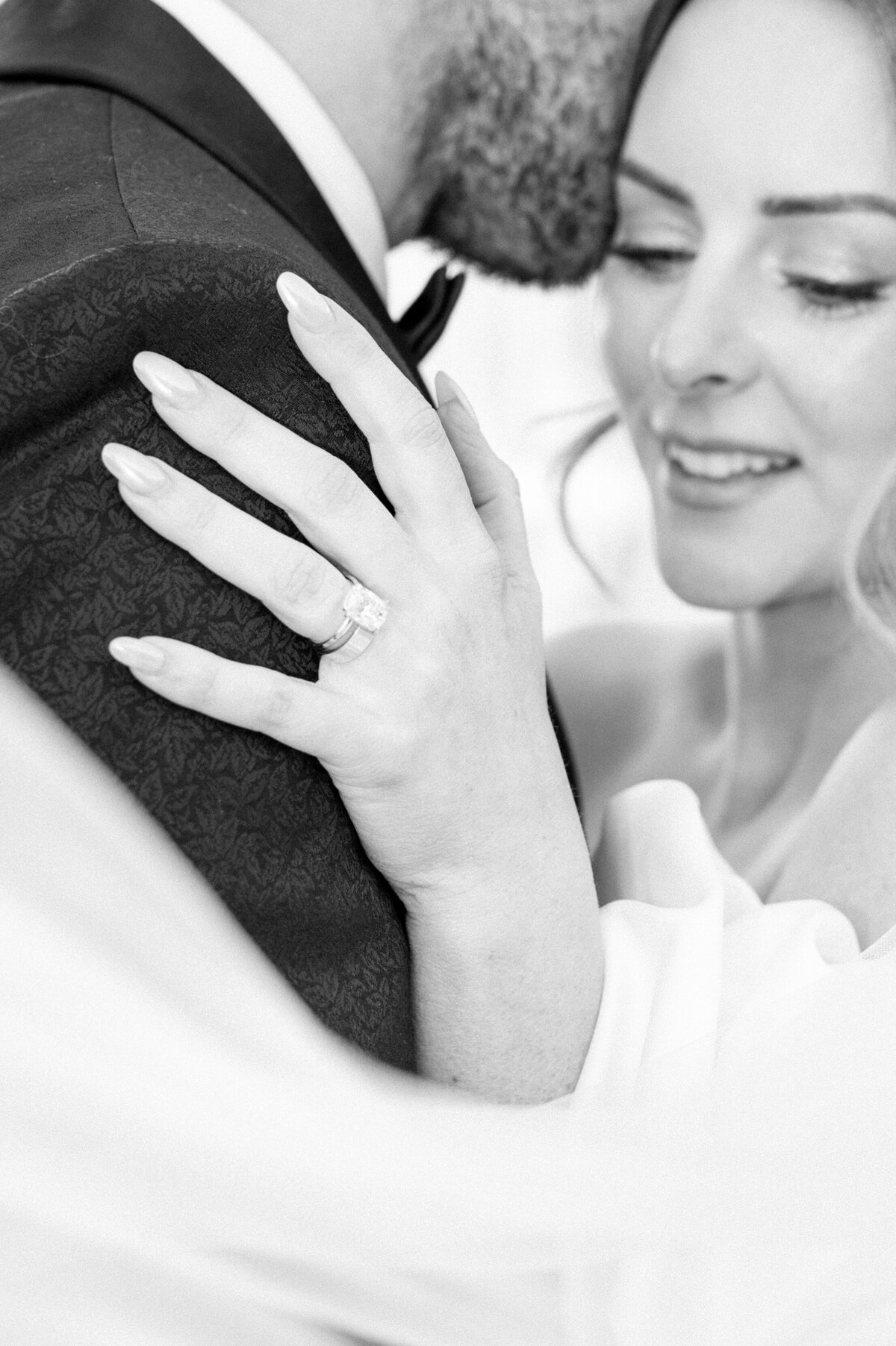Closeup of bride’s engagement ring and groom’s suit during an intimate embrace