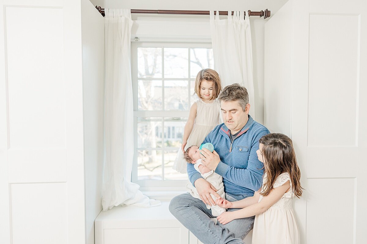 dad sits in window with children dung in-home newborn photo session with Sara Sniderman Photography in Needham Massachusetts