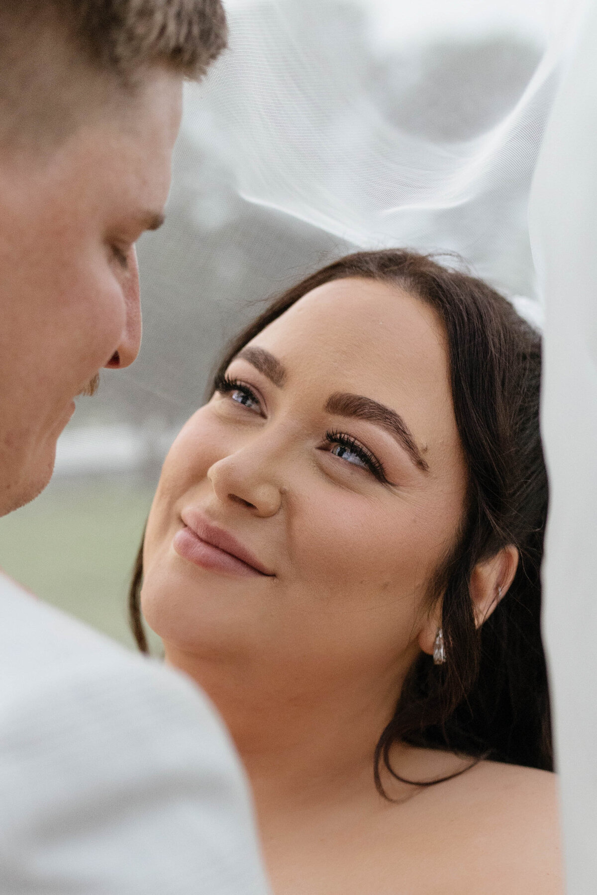 Newlyweds looking into each other's eyes underneath a veil. 