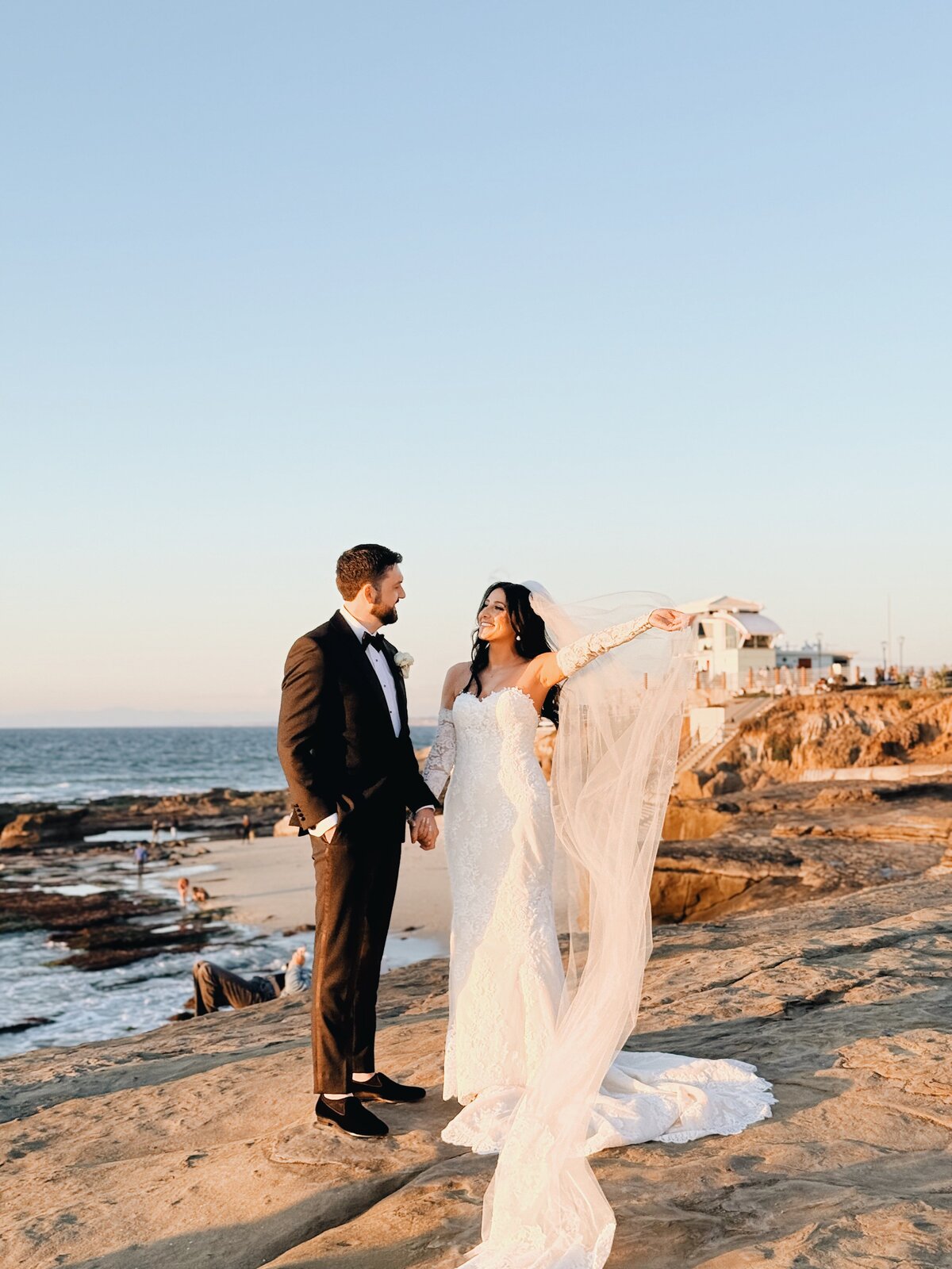 Bride and groom holding hands and letting the veil flow on the cliffs of La Jolla Beach in San Diego, California.