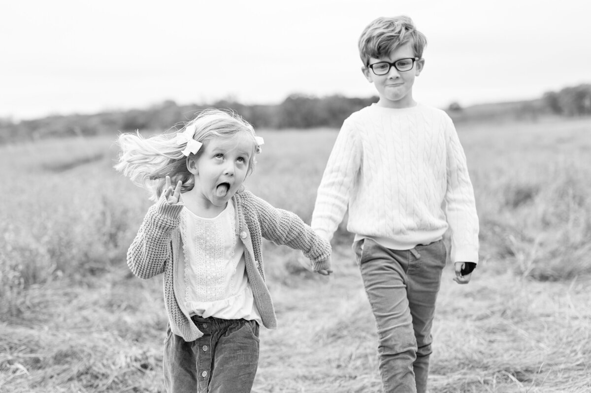 Portrait in black and white or siblings walking together, with little girl making a silly face