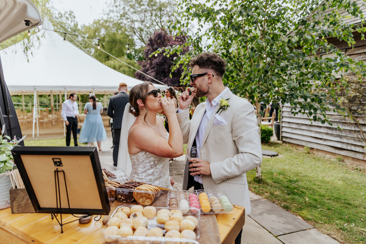 Bride and groom wearing sunglasses look at eachother while biting into a macaron