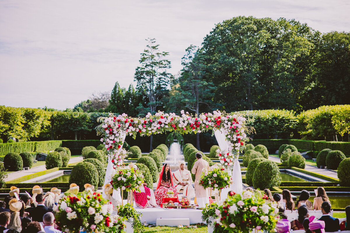 An indian bride and groom listening to the priest during the hindu ceremony on their wedding day under the mandap at oheka castle