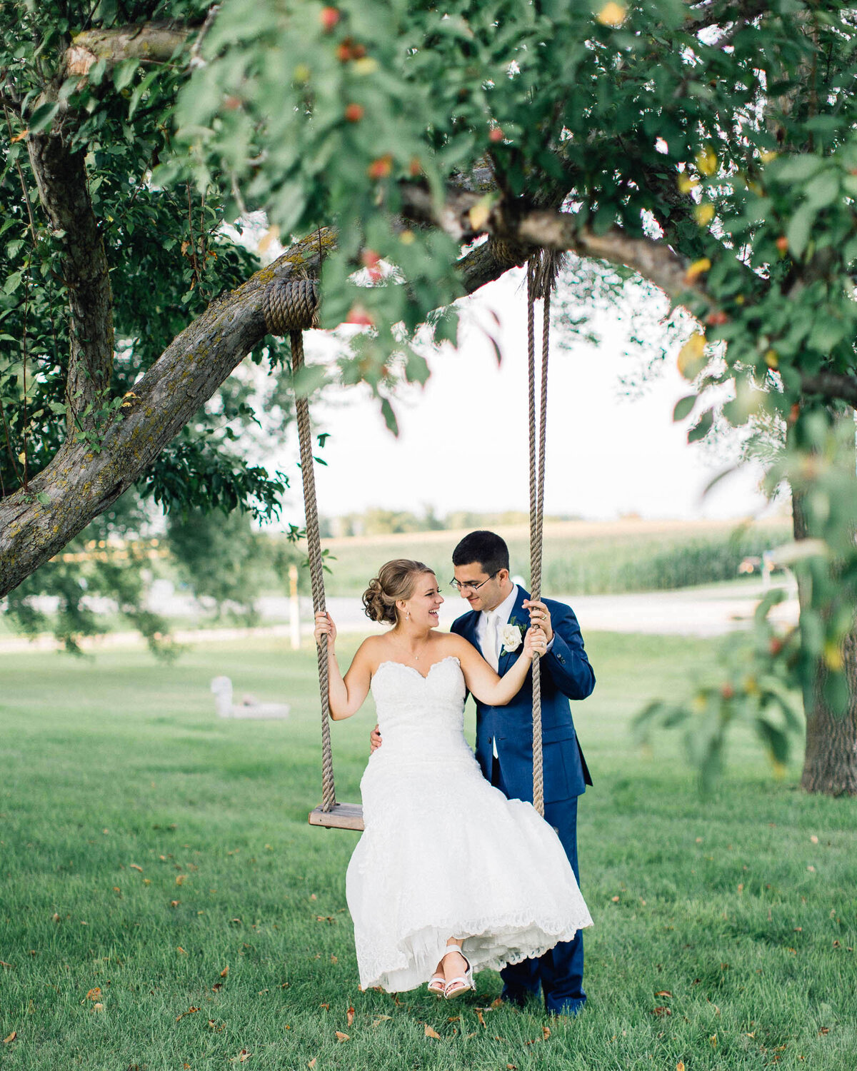 Bride sitting on a swing laughing while the groom stands behind her, gently swinging her and looking at her at The Cottage Farmhouse, captured by Toly Dzyuba Photography.