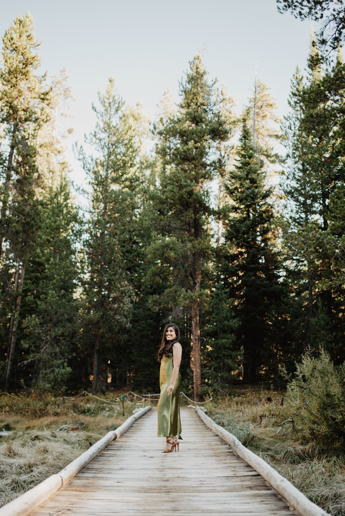 woman posing in Jackson Hole on a wooden dock trail with the woods behind her for a formal session
